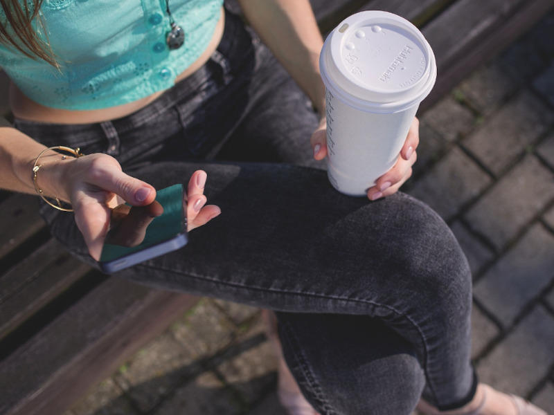 Jugendliche Person mit Smartphone und Getränk